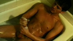 Gorgeous young man gets in a soapy bath to stroke his long pole